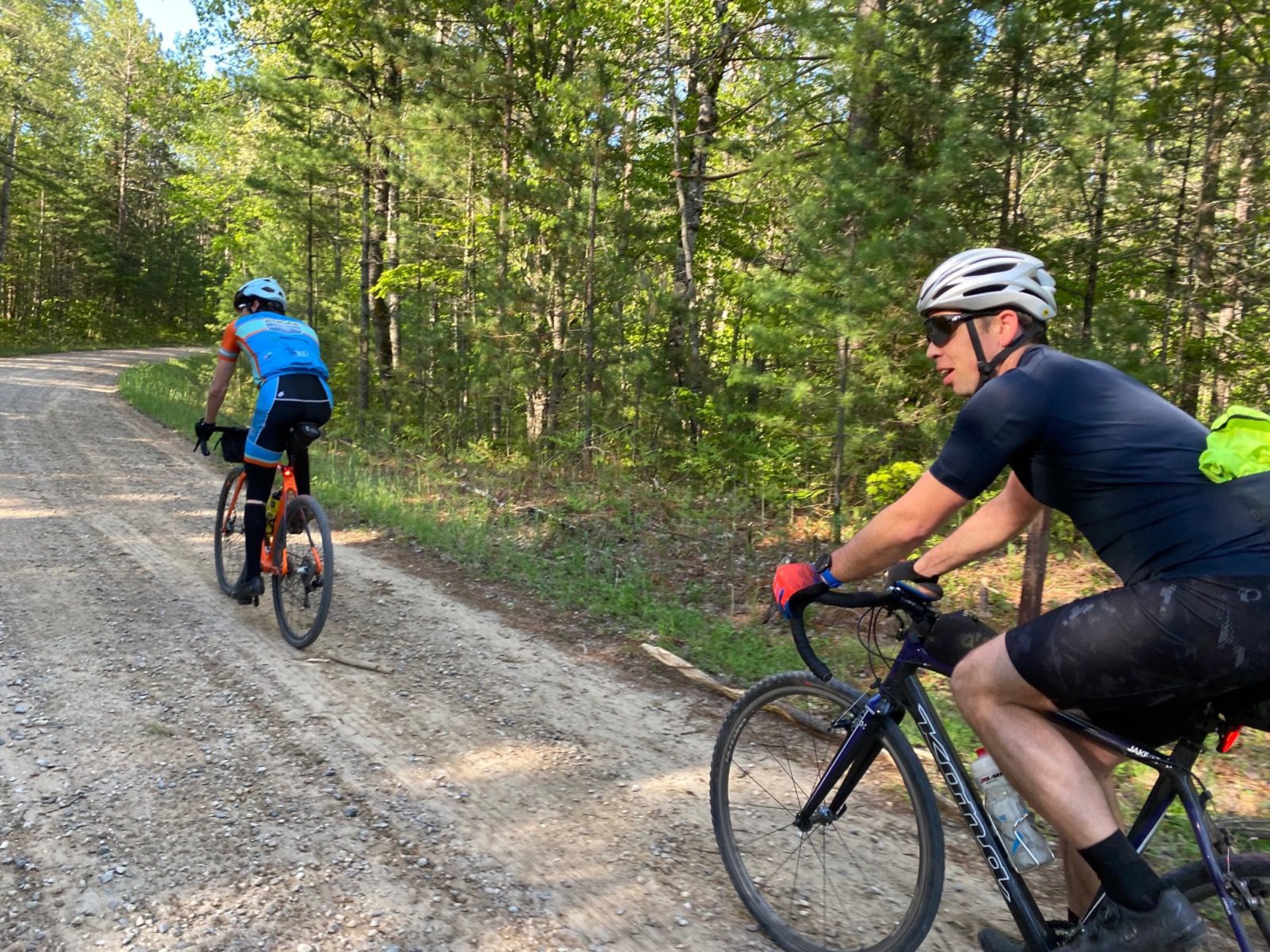 Two gravel cyclists riding on a pine-lined road during Hiawatha's Revenge.